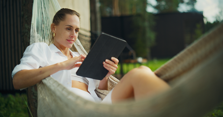 Woman relaxing in a garden hammock reading on a tablet, researching TMS for anxiety in Colorado Springs