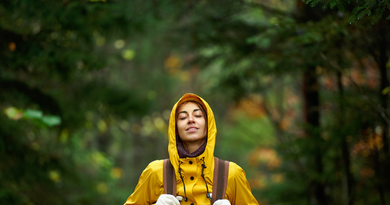 Woman in a yellow jacket standing with eyes closed in an autumn forest, TMS for depression in Colorado Springs