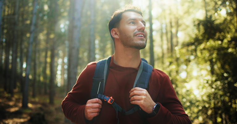 Hiker with a backpack smiling on a sunlit forest trail, TMS for teens and adolescents in Colorado Springs